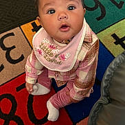 Kalani is registered to the contest to win money with this photo: baby, child, infant, plaid_clothing, pink, bib, socks, play_mat, numbers, letters, curious, wide_eyes, sitting, indoors, floor, cute, portrait, person, young_child, colorful