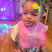 Diara is registered to the contest to win money with this photo: baby, blanket, box, child, clothing, colorful_lights, cute, expression, fan, floor, hair_clips, holding, indoor, person, pink_bib, room, standing, toddler, wooden_floor, young