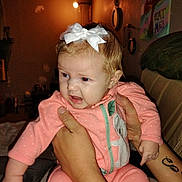 Bailey joined the competition — help win amazing prizes! baby, infant, pink_onesie, white_bow, tattooed_arms, indoor, warm_lighting, wall_art, child, person, holding, expression, face, cute, room, furniture, decor, headwear, clothing, portrait