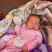 Hazel is registered to the contest to win money with this photo: baby, newborn, sleeping, blanket, pink_clothing, onesie, couch, soft_texture, hand, face, peaceful, indoor, floral_pattern, infant, cute, resting, child, warm, cozy, portrait