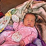 baby, newborn, sleeping, blanket, pink_clothing, onesie, couch, soft_texture, hand, face, peaceful, indoor, floral_pattern, infant, cute, resting, child, warm, cozy, portrait