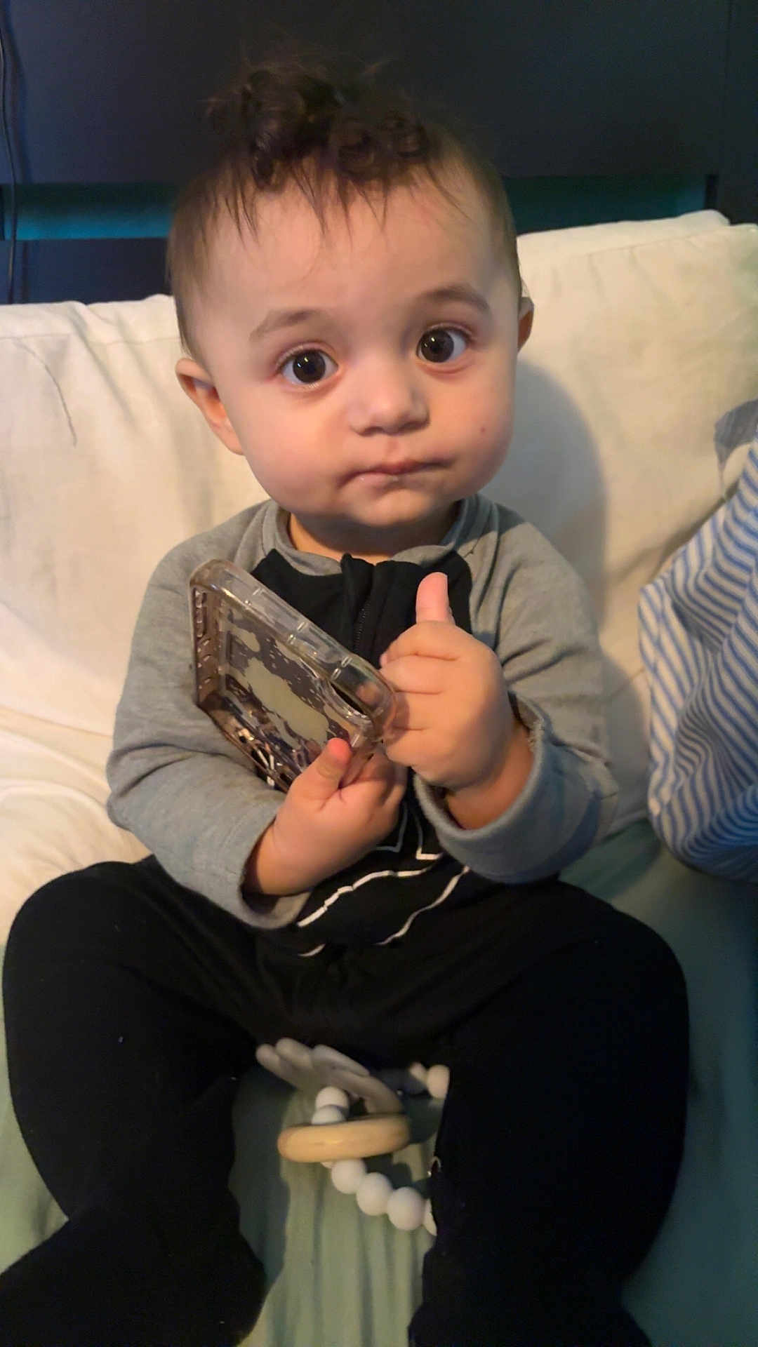 Tatum joined the competition — help win amazing prizes! child, baby, toddler, big_eyes, holding_phone, phone_case, onesie, sitting, couch, pillow, toy, teether, hand, face, portrait, indoors, blanket, curly_hair, serious_expression, cute