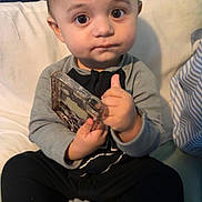 Tatum joined the competition — help win amazing prizes! child, baby, toddler, big_eyes, holding_phone, phone_case, onesie, sitting, couch, pillow, toy, teether, hand, face, portrait, indoors, blanket, curly_hair, serious_expression, cute