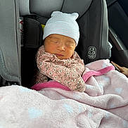 Penelope is registered to the contest to win money with this photo: baby, newborn, car_seat, blanket, sleeping, hat, floral_clothing, pink, cozy, child, infant, seatbelt, car_interior, soft_texture, cute, peaceful, wrapped, warm, child_seat, portrait