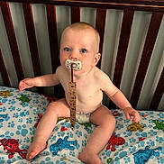 Oakley is registered to the contest to win money with this photo: baby, baby_clothing, baby_toy, bedding, blue_eyes, child, child_bed, crib, curious, cute, diaper, indoors, infant, pacifier, pale_skin, plush_bedding, robot_pattern, short_hair, sitting, wooden_crib