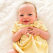Lily is registered to the contest to win money with this photo: baby, infant, yellow_dress, smile, hands, blue_eyes, soft_blanket, cute, newborn, lying_down, happy, skin, portrait, child, young, adorable, cozy, fuzzy_background, peaceful, small_fingers