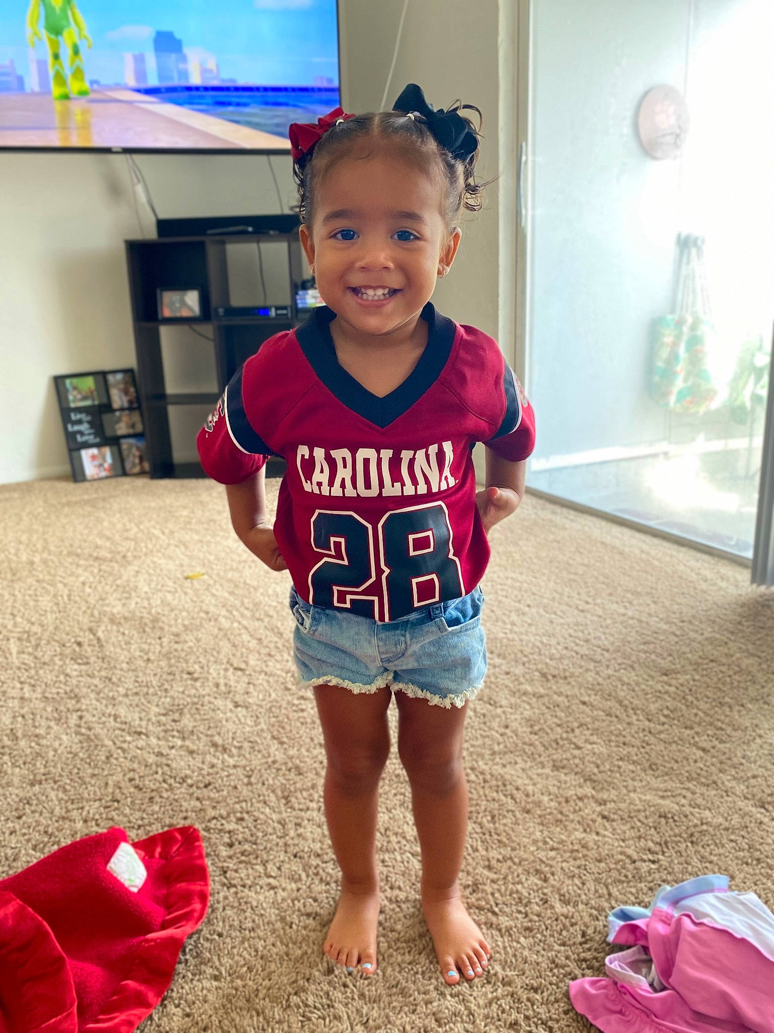 Teagan joined the competition — help win amazing prizes! baby_toddler_clothing, blue, child, face, floor, flooring, fun, hair, happy, human_leg, joy, person, red, shorts, sleeve, smile, sportswear, standing, t_shirt, television