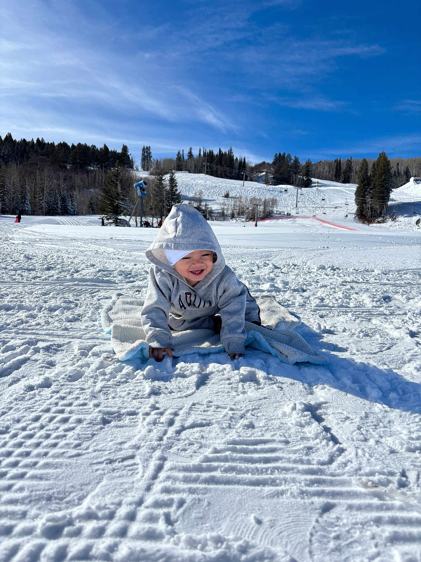Messi is registered to the contest to win money with this photo: toddler, child, snow, blanket, hoodie, winter, outdoor, sky, trees, hill, smiling, cold, play, crawling, nature, daytime, recreation, fun, clothing, landscape
