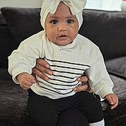 Ohana a rejoint le concours — aidez-le/la à gagner de superbes lots ! baby, black_pants, bow, child, couch, cozy, curious, face, hands, headband, home_interior, indoor, person, portrait, sitting, socks, soft_light, striped_clothing, sweater, window