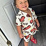 Malekhi is registered to the contest to win money with this photo: toddler, child, curly_hair, smiling, standing, indoors, door, white_door, racing_cars, checkered_flags, shorts, shirt, red_sandals, flooring, happy, cute, clothing, person, portrait, young_child