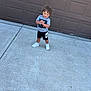Malekhi joined the competition — help win amazing prizes! child, toddler, curly_hair, standing, sidewalk, garage_door, concrete, sneakers, nike, shorts, tshirt, outdoor, happy, smiling, person, casual_clothing, daylight, young_child, playful, cute