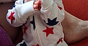 Sammuel is registered to the contest to win money with this photo: baby, infant, child, portrait, sitting, hands, face, eyes, onesie, stars, red, white, blue, couch, indoor, adult_arm, tattoo, close_up, playful, family