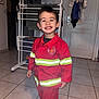 Thomas participe au concours pour gagner de l'argent avec cette photo : child, smile, firefighter_costume, red_clothing, indoor, tiled_floor, drying_rack, socks, door, happy, person, portrait, floor, clothing, boy, home, casual, cute, young, standing