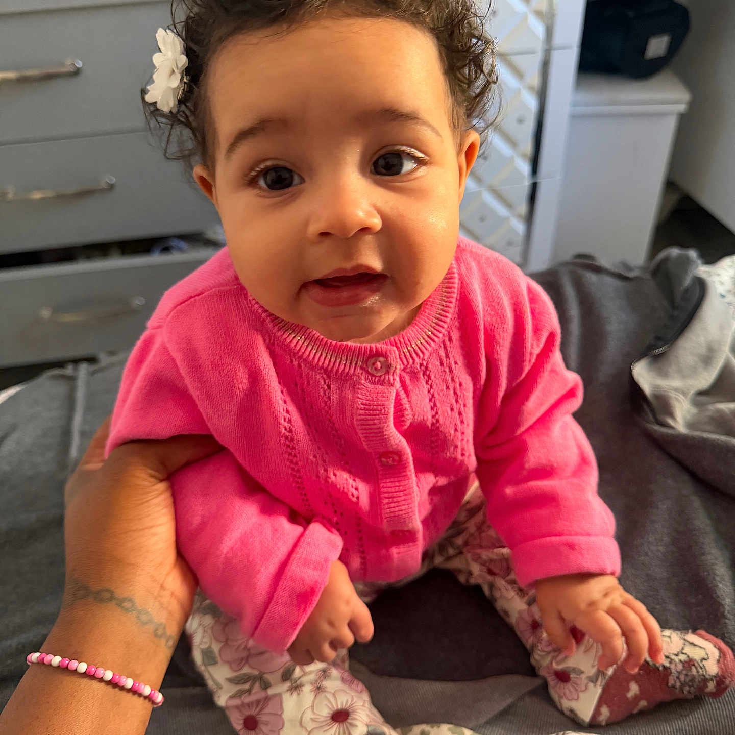 Althea participe au concours pour gagner de l'argent avec cette photo : baby, bed, blanket, bracelet, child, cozy, curly_hair, cute, face, floral_pants, flower_hair_accessory, hand_support, indoor, person, pink_sweater, portrait, sitting, smiling, soft_lighting, tattoo