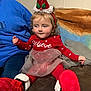 child, red_clothing, santa_hat, holiday, toddler, indoor, couch, festive, boots, tulle_skirt, person, cute, holiday_season, smiling, headwear, plush, cozy, home, sitting, young_child