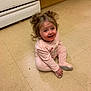 toddler, child, baby, curly_hair, pink_onesie, smiling, sitting, kitchen_floor, floor_tiles, happy, indoor, young_child, cute, person, infant, playful, hair_buns, childhood, expression, home