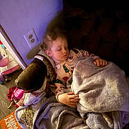 Nevaeh is registered to the contest to win money with this photo: child, sleeping, blanket, couch, indoor, cozy, pajamas, face, hand, relaxing, soft_lighting, furniture, floor, toy, purple, brown, comfort, peaceful, young_child, home