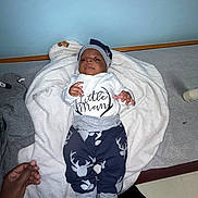 Jermaine joined the competition — help win amazing prizes! baby, blanket, blue_wall, bottle, calm, carpet, child, clothing, cute, deer_pattern, floor, hand, hat, indoors, infant, lying_down, pants, person, socks, white_blanket