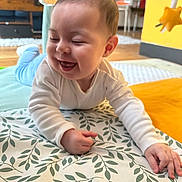Mathias a rejoint le concours — aidez-le/la à gagner de superbes lots ! baby, child, smiling, happy, indoor, mat, leaf_pattern, white_clothing, blue_pants, hand, face, head, floor, toy, yellow_wall, wooden_floor, furniture, home, cute, playtime