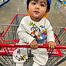 toddler, child, shopping_cart, costco, warehouse, cap, blue_cap, white_outfit, disney_characters, goofy, donald_duck, mickey_mouse, socks, floor, aisle, handrail, curious_expression, indoor, store, person