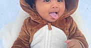 Veer is registered to the contest to win money with this photo: baby, child, onesie, hood, animal_costume, brown, white, cute, tongue_out, playful, blanket, snow, winter, outdoor, infant, smile, face, hand, warm_clothing, portrait