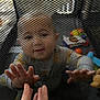 James is registered to the contest to win money with this photo: baby, child, mesh, hand, fingers, toys, playpen, indoor, person, curious, reaching, colorful, soft_lighting, closeup, crawling, carpet, interaction, young_child, baby_clothes, parent_hand