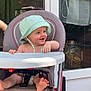 baby, child, high_chair, hat, smiling, barefoot, outdoor, window, glass_door, seat, foot, playful, happy, person, infant, sunlight, home, furniture, diaper, curtain