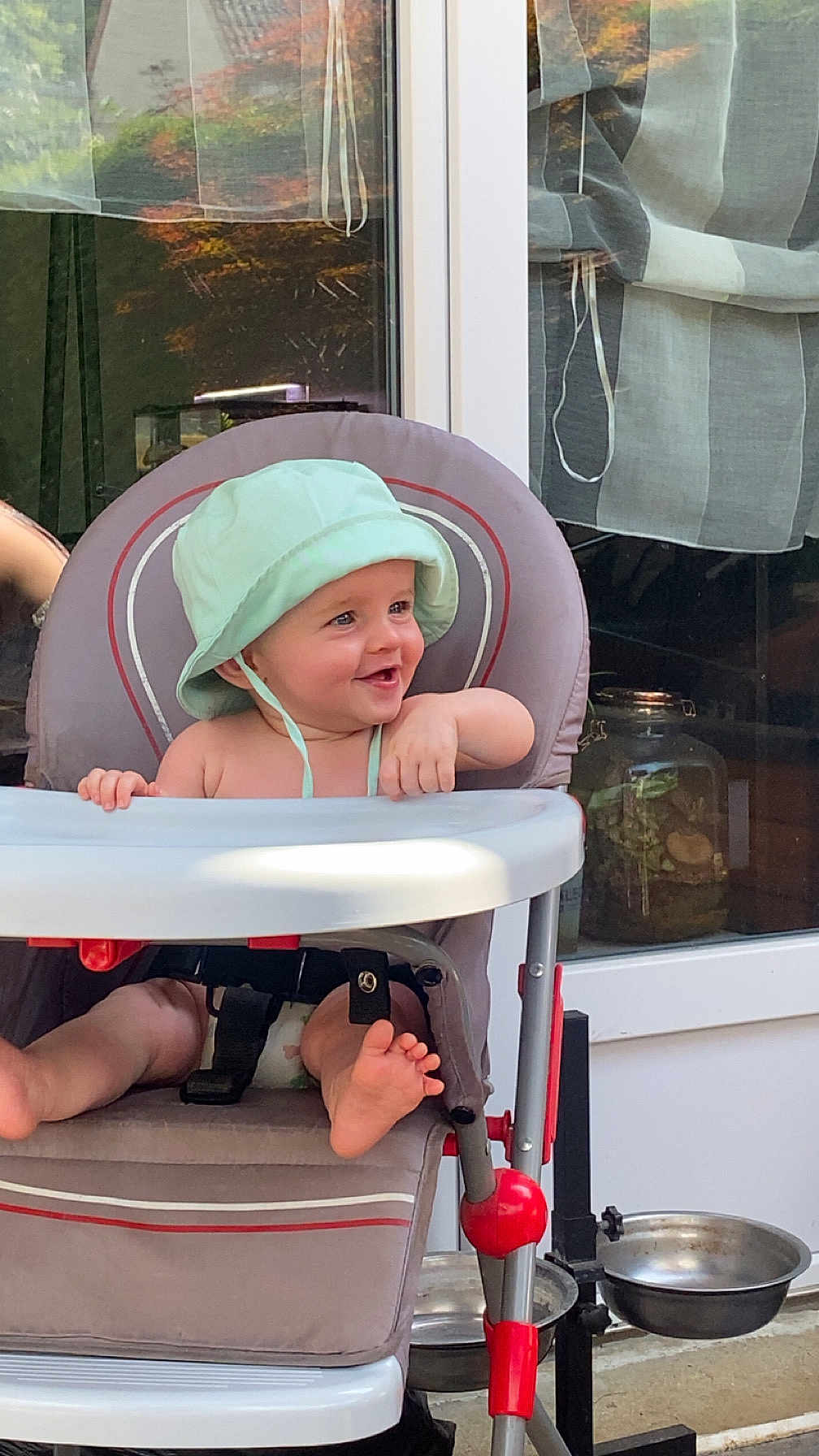Aleks a rejoint le concours — aidez-le/la à gagner de superbes lots ! baby, child, high_chair, hat, smiling, barefoot, outdoor, window, glass_door, seat, foot, playful, happy, person, infant, sunlight, home, furniture, diaper, curtain