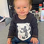 toddler, child, smile, face, sitting, mickey_mouse, shirt, jeans, socks, hand, kitchen, counter, door, container, cup, table, indoor, person, clothing, happy