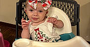 Gracie is registered to the contest to win money with this photo: baby, bow, child, clothing, cute, earrings, electrical_outlet, happy, high_chair, indoor, infant, person, playful, seat, smile, table, tongue_out, wall, watermelon_pattern, wood_floor