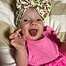 baby, child, infant, tongue, headband, pink_dress, smiling, happy, playful, bed, striped_bedspread, hand, cute, portrait, person, young, indoors, apparel, fabric, expression
