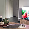 cat, table, wooden_table, gray_cat, white_cat, decorative_pumpkins, ceramic_pumpkins, living_room, tv, television, floor, door, interior, home, relaxed_cat, resting_cat, indoor, furniture, modern, quiet