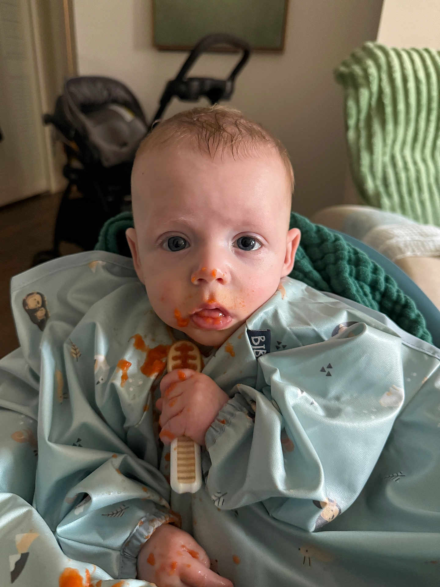 Mayer joined the competition — help win amazing prizes! baby, messy_face, bib, teething_toy, food_stains, blue_clothing, indoor, blanket, stroller, curious_eyes, child, sitting, infant, hand, mouth, face, person, portrait, young_child, home