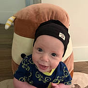 Mayer joined the competition — help win amazing prizes! baby, infant, smiling, hat, beanie, blue_shirt, bicycle_pattern, hands, plush_pillow, animal_pillow, indoor, carpet, person, cute, happy, child, face, headwear, holding, home