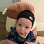 baby, infant, smiling, hat, beanie, blue_shirt, bicycle_pattern, hands, plush_pillow, animal_pillow, indoor, carpet, person, cute, happy, child, face, headwear, holding, home
