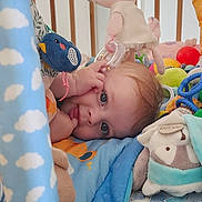 éléanor a rejoint le concours — aidez-le/la à gagner de superbes lots ! baby, blue_eyes, rattle, stuffed_animal, plush_toy, crib, blanket, colorful, play_area, soft_toys, child, infant, cute, tongue_out, hand, face, lying_down, indoors, playtime, happy