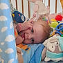 baby, blue_eyes, rattle, stuffed_animal, plush_toy, crib, blanket, colorful, play_area, soft_toys, child, infant, cute, tongue_out, hand, face, lying_down, indoors, playtime, happy