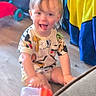 toddler, child, sippy_cup, tongue_out, floor, toy, colorful, living_room, happy, smiling, short_hair, casual_clothing, wooden_floor, playful, indoor, person, seat, couch, blanket, furniture