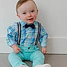 baby, blue_clothing, bow_tie, boy, casual, child, cute, fashion, floor, happy, indoor, infant, person, plaid_shirt, portrait, sitting, smiling, suspenders, white_wall, young