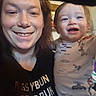 Kayn is registered to the contest to win money with this photo: adult, baby, casual, child, closeup, clothing, expression, face, family, happy, indoor, joy, light, person, portrait, printed_shirt, selfie, smile, text_on_shirt, toddler