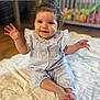 baby, child, smiling, waving, sitting, blanket, curly_hair, blue_outfit, indoors, crib, wooden_floor, happy, cute, person, infant, face, foot, hand, room, soft_light