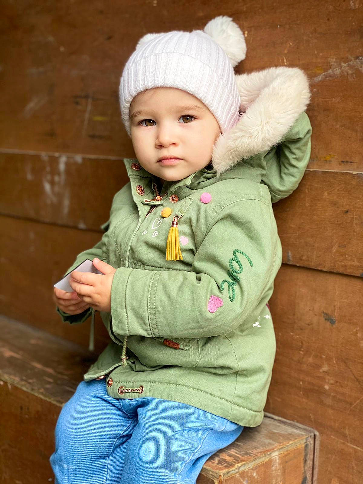 Irene is registered to the contest to win money with this photo: baby, baby_toddler_clothing, cap, child, eye, face, fur, happy, head, headgear, headwear, human_body, jacket, jeans, person, skin, sleeve, toddler, tree, wood