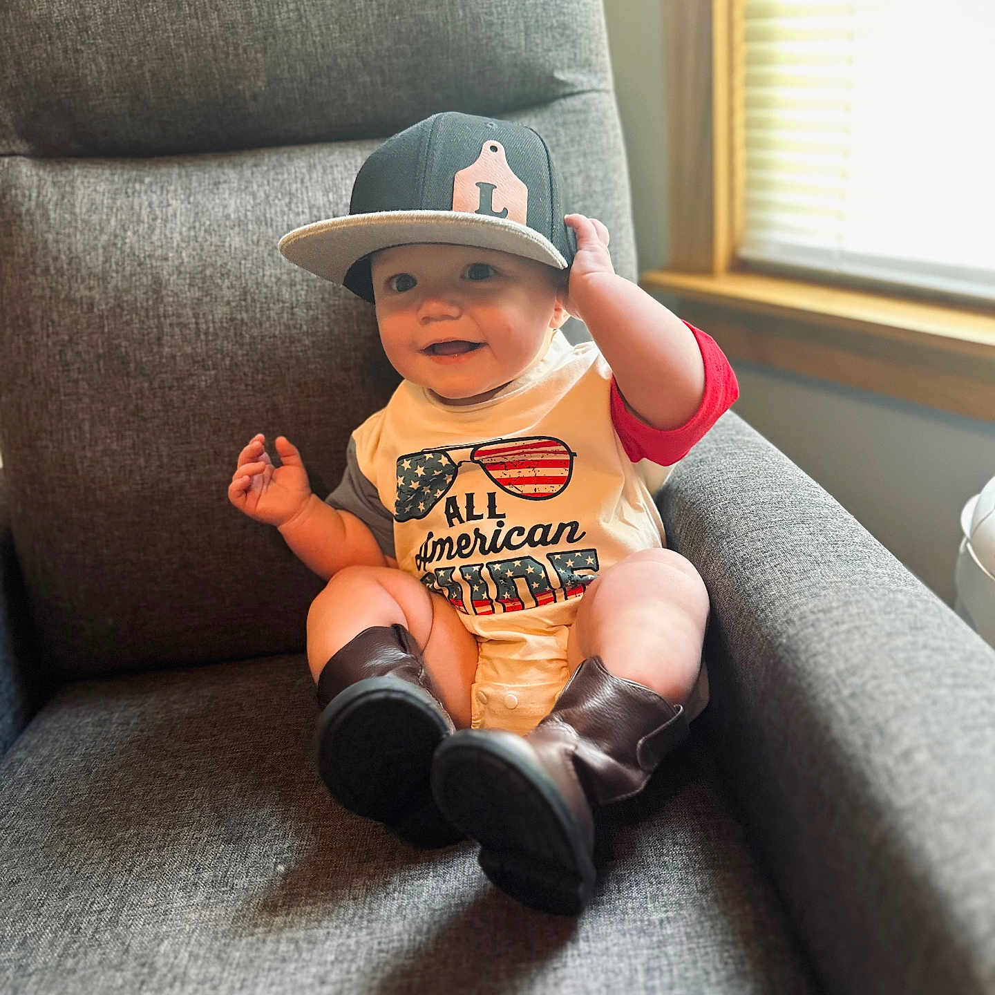 Lucas is registered to the contest to win money with this photo: armchair, baby, boots, cap, child, clothing, cute, furniture, hand, happy, hat, indoor, infant, legs, light, person, shirt, sitting, smile, window