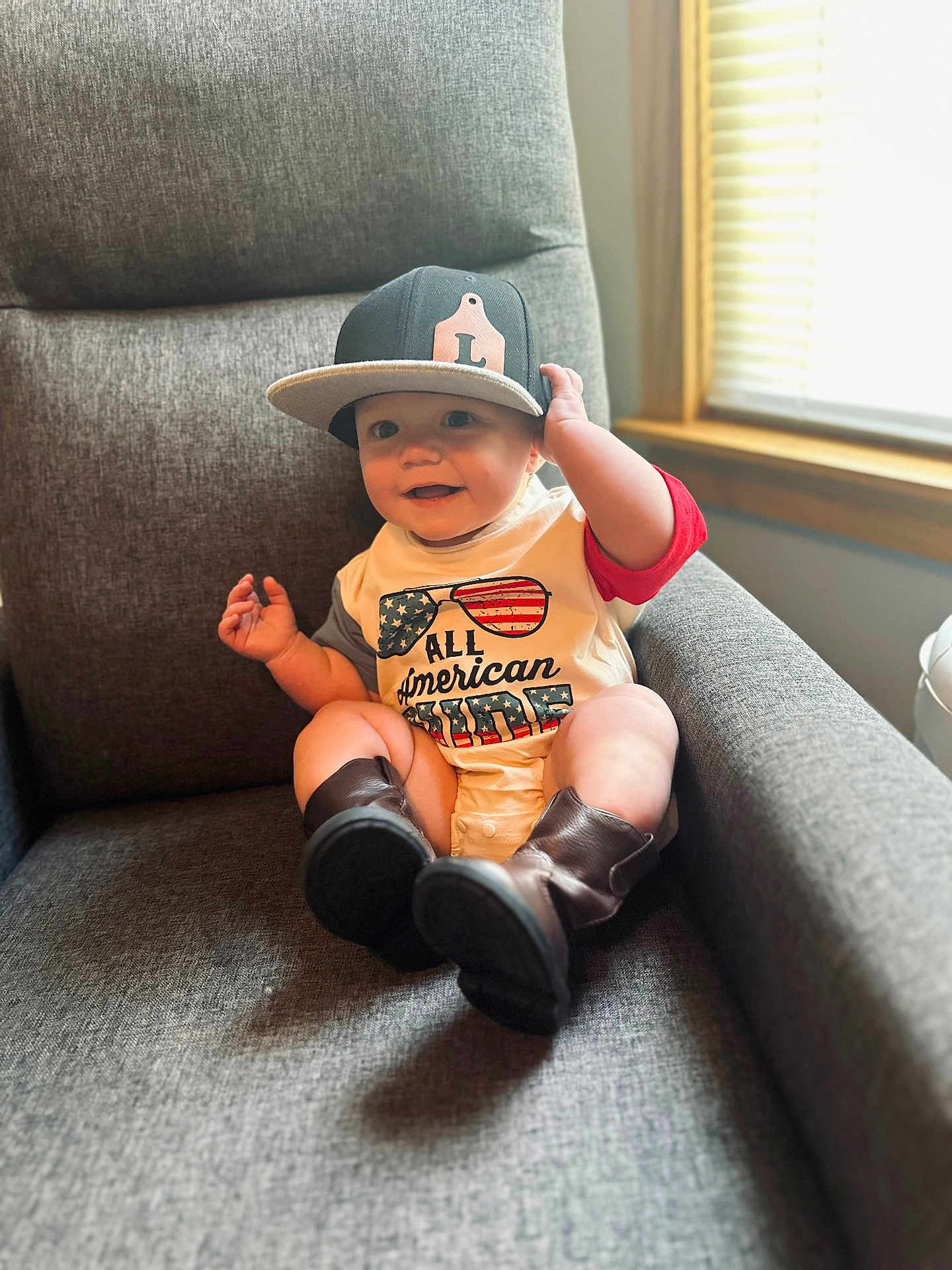 Lucas is registered to the contest to win money with this photo: baby, child, cap, hat, shirt, boots, armchair, smile, indoor, window, light, happy, clothing, person, infant, furniture, legs, hand, sitting, cute