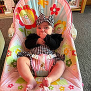 Bonnie-Rae joined the competition — help win amazing prizes! baby, infant, child, fisher_price, baby_chair, headband, black_and_white_clothing, hand_in_mouth, colorful, flower_pattern, bee_pattern, indoor, carpet, furniture, photo_frame, living_room, cute, seated, person, smiling