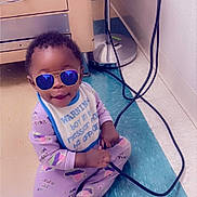 Jahsir is registered to the contest to win money with this photo: baby, bib, black_cable, blue, cabinet, cable, child, cute, floor, indoor, lamp, pajamas, person, playful, purple, reflection, smiling, sunglasses, toddler, wall