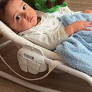 Aiden a rejoint le concours — aidez-le/la à gagner de superbes lots ! baby, infant, child, blanket, plush_toy, turtle, baby_rocker, floor, wooden_floor, indoor, child_wearing_white, soft_toy, curious_expression, reclining, furniture, home, comfort, resting, cute, portrait