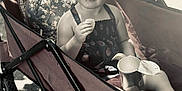 Mary-Alice is registered to the contest to win money with this photo: toddler, child, smiling, wagon, snack, chip, backpack, outdoor, sunlight, shadow, curly_hair, happy, black_and_white, dress, seat, playtime, food, container, summer, portrait