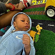 Hezekiah joined the competition — help win amazing prizes! baby, child, hoodie, nike, pacifier, toy, yellow_toy, colorful_mat, carpet, hand, leg, person, indoor, casual, footwear, sneaker, curious, infant, playtime, relaxed