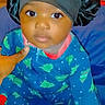 Xamira is registered to the contest to win money with this photo: baby, child, infant, onesie, blue_clothing, christmas_tree_pattern, black_bonnet, satin_bonnet, sitting, hand, indoor, portrait, cute, looking_at_camera, young_child, soft_lighting, close_up, person, footwear, white_sock